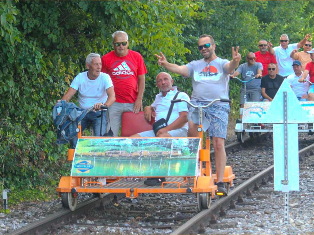 Mitarbeiter der aSTIFTERbau GmbH auf einer Draisine, lächelnd und mit dem Friedenszeichen, während des Betriebsausflugs.